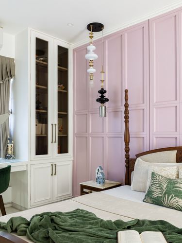 Bedroom corner with pink paneled wall, glass cabinet, and layered pendant lights over four-poster bed