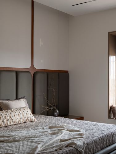 Bedroom corner with grey channel headboard, wood cross frame, and bedside niche window