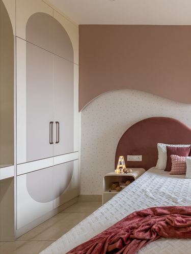 Bedroom corner with curved cream wardrobe, dotted wallpaper, and rose velvet arched headboard