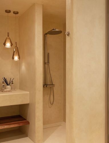 Recessed plaster shower niche with rainfall head beside a floating stone vanity and pendant lights