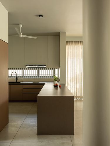 Minimalist kitchen with terracotta cabinetry and island seen past a curved wall, soft daylight from sheer curtain