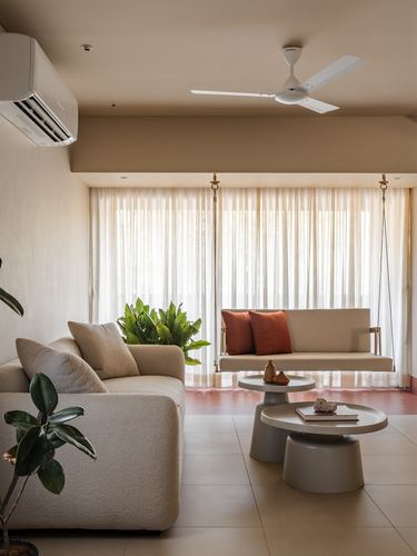 Neutral living room with boucle sofa, hanging swing, and terracotta cushions before sheer curtains