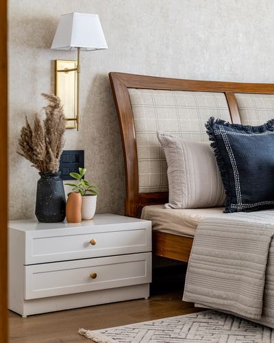 Bedroom corner with white nightstand, brass sconce, pampas vase and wooden upholstered headboard with navy cushion