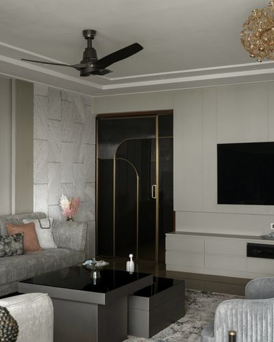 Grey living room with textured stone wall, brass-arched glass sliding door, black coffee table and TV console.