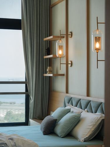 Bedroom corner with sage headboard, brass wall sconces, floating wood shelves, and city view through curtains
