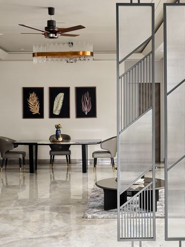 Dining area seen past a fluted glass partition, with black table, grey chairs, and brass-ringed pendant light