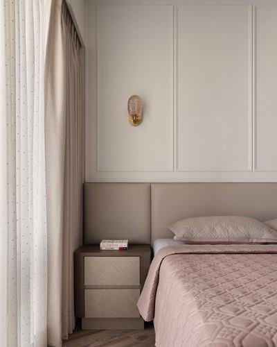 Beige paneled bedroom wall with brass sconce, wood nightstand, and pink quilted bed