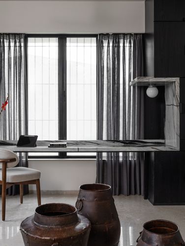Marble desk niche by curtained window with vintage metal urns in foreground