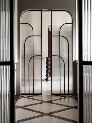 Symmetrical arched glass and metal doors frame a hallway with a ball-chain pendant beyond