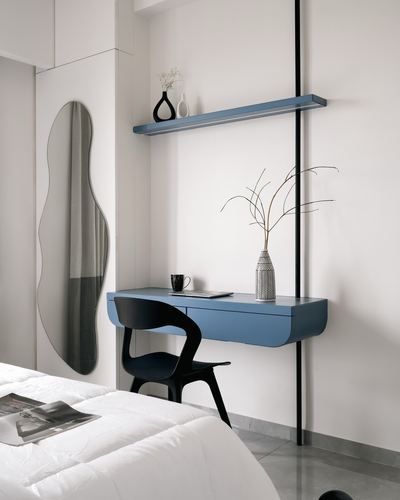 Wall-mounted blue desk and shelf beside an irregular mirror in a minimalist bedroom