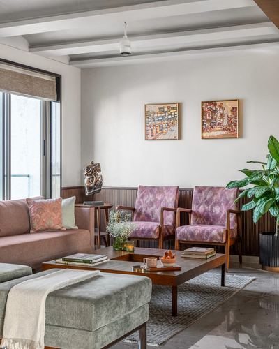 Living room with pink sofa, mauve armchairs, fluted wood paneling and beamed ceiling