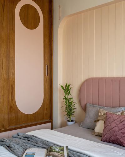Bedroom corner with wood wardrobe featuring pink oval inlay and pink tufted headboard against fluted pastel wall