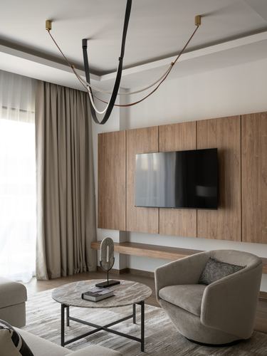 Neutral living room with wood-paneled TV wall, round marble table, and curved swivel armchair