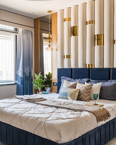 Bedroom with fluted cream and brass headboard panel above a navy velvet bed with layered pillows