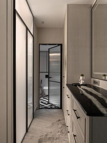 Narrow hallway with glass sliding doors leads to a black-framed glass bathroom door, black marble vanity on the right.