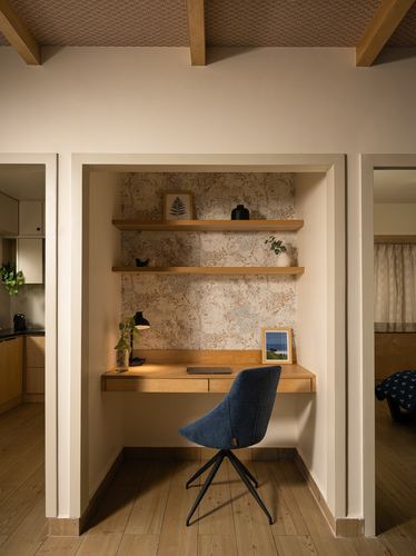 Built-in study nook with floating wood desk, patterned wallpaper, open shelves, and blue swivel chair.