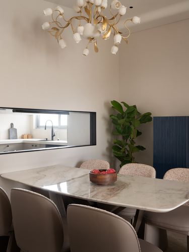 Dining room with marble table, floral chandelier, and window into kitchen