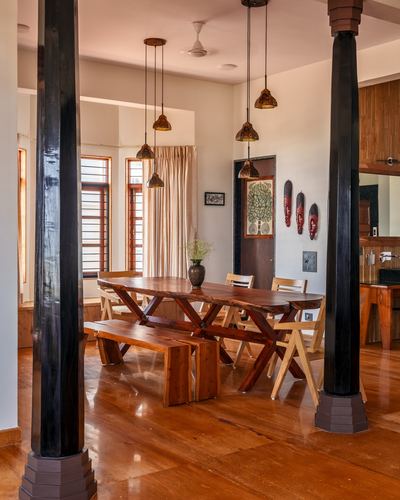 Wooden dining room with live-edge table, black columns, and clustered pendant lights in a Goan home
