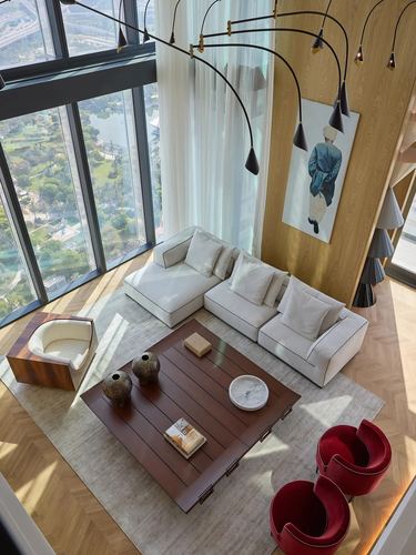Aerial view of a double-height living room with floor-to-ceiling windows, white sectional, arced chandelier and red velvet chairs.