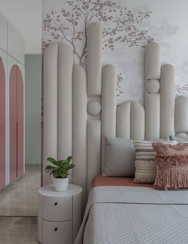 Bedroom with sculptural tubular beige headboard against tree mural, blush arched wardrobe, round nightstand