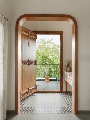 Arched wooden doorway with carved traditional door opening to a green balcony, patterned floor tiles in foreground