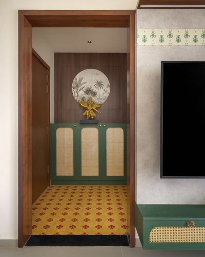 Foyer view through wooden doorway showing green cane cabinet, brass figurine, and patterned yellow tile floor.