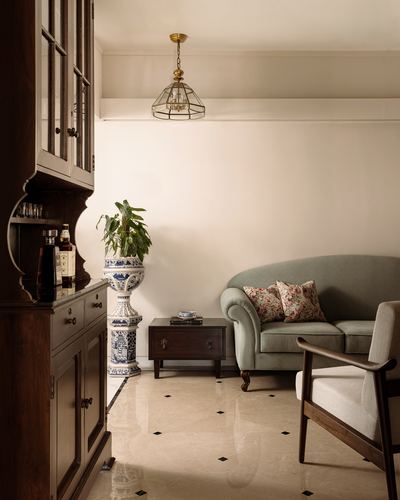 Living room corner with dark wood cabinet, porcelain planter, green sofa and marble floor