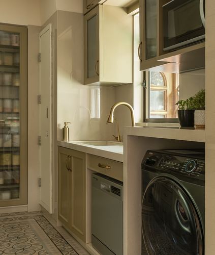 Compact utility kitchen with brass faucet, olive cabinets, washing machine, and patterned cement floor