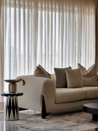 Beige sofa with patterned cushion beside geometric black-and-white side table against sheer curtains