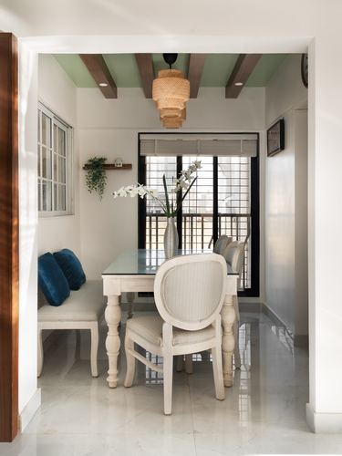 Dining nook with beamed sage ceiling, cane pendant light, bench and carved chairs around marble table