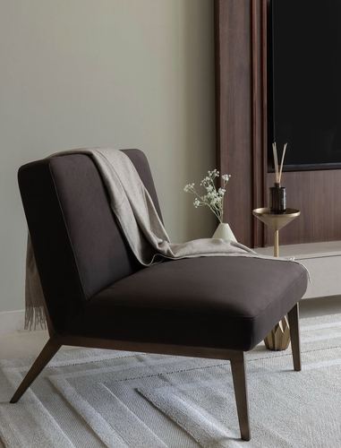 Dark brown velvet armchair with taupe throw beside a brass side table and wood panelling