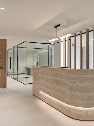 Curved stone reception desk beside glass-walled office with wood fluted screen in modern lobby
