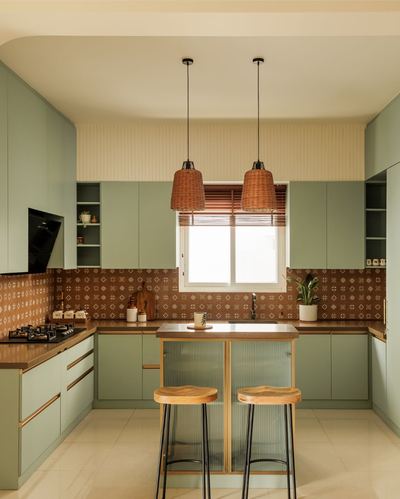 Sage-green U-shaped kitchen with patterned terracotta backsplash, island, and two woven pendant lights