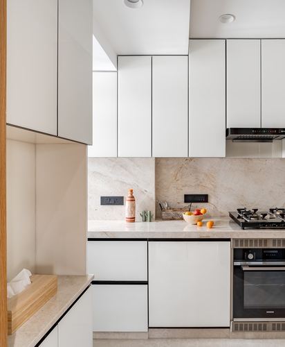 Minimalist white kitchen with stone backsplash, gas hob, built-in oven, and fruit bowl on counter