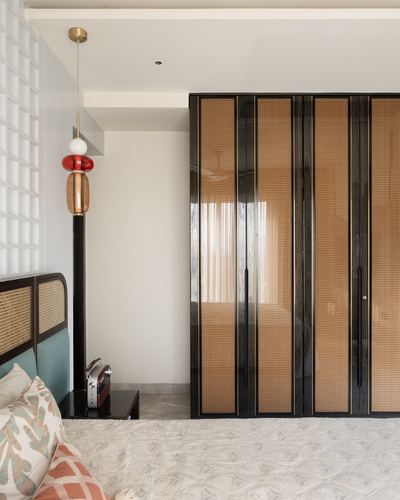 Bedroom corner with caned wardrobe, brass pendant lamp, and cane headboard bed