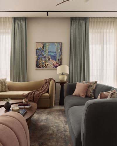 Living room with mustard sofa, grey sofa, pink ottoman, and framed art between sage curtains