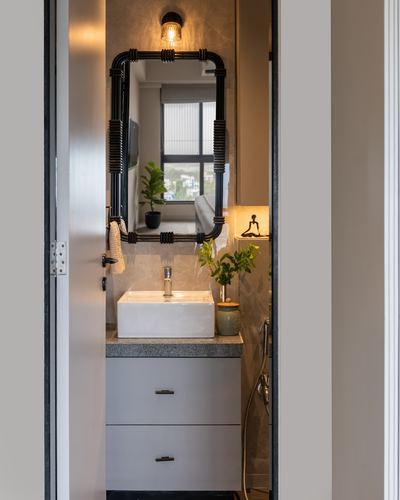 Bathroom vanity with wrapped-frame mirror seen through open doorway, plants and warm light