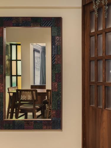 Patterned tile-framed mirror reflecting a dining area beside a wooden glass-paned door