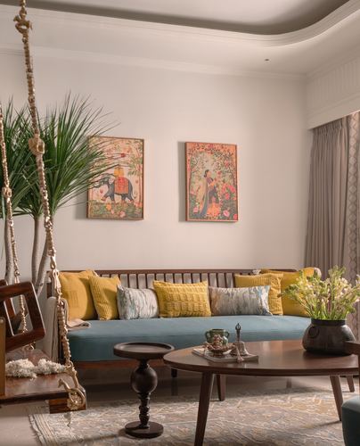 Living room with teal sofa, mustard cushions, Indian miniature art, and a wooden hanging swing