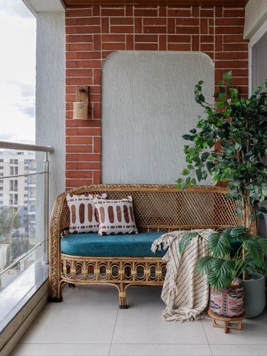Cane sofa with teal cushions on a balcony against a brick wall and plants