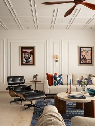Living room with paneled walls, black Eames lounge chair, cream sofa and round marble-top coffee table