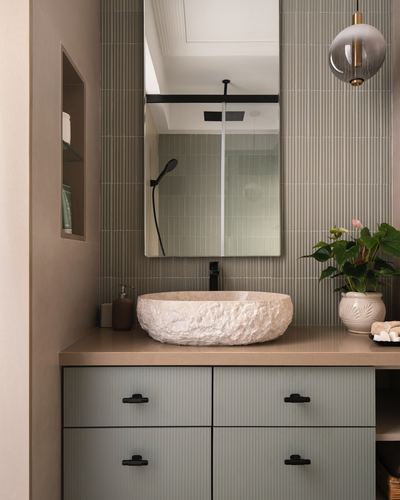 Bathroom vanity with carved stone basin, ribbed tile wall, mirror and globe pendant