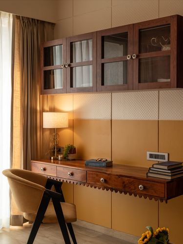 Wooden study desk with scalloped edge below mustard-paneled wall and glass cabinets