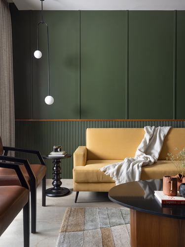 Mustard sofa against dark green paneled wall with turned side table and leather armchair