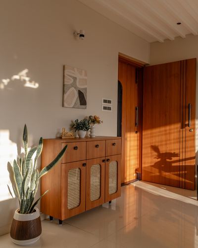 Sunlit foyer with wooden entry door and cane-front console cabinet against neutral wall
