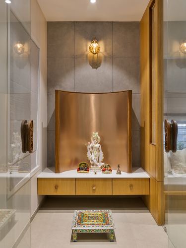 Pooja niche with curved copper backdrop, deity idol, and floating wooden drawer unit