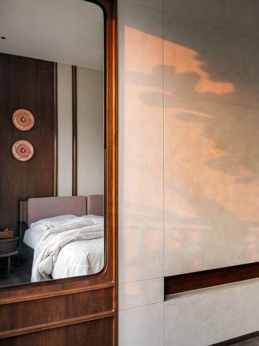 Wood-framed mirror reflecting a bedroom beside a stone wall with warm sunset light
