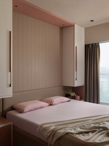 Pastel pink bedroom with fluted wood headboard wall and overhead storage cabinets beside a window.