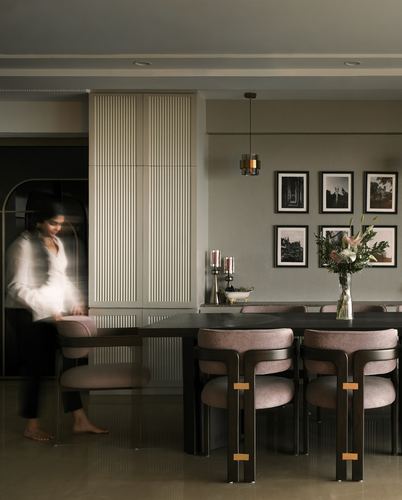 Woman pulling out a mauve upholstered dining chair beside a fluted cabinet and gallery wall