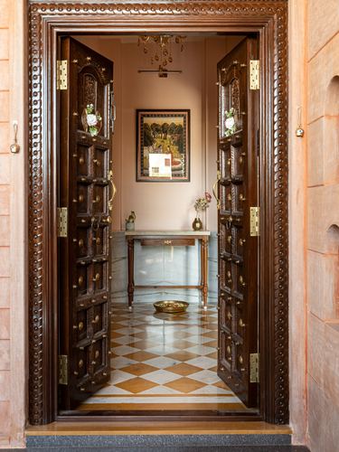 Carved wooden double doors open onto a marble-floored foyer with a console table and framed painting